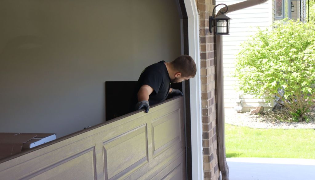 white male technician installs beige garage door panel