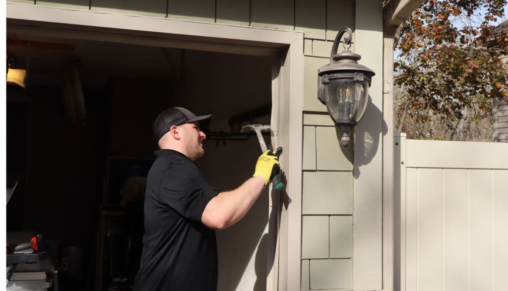 technician uses hammer to make adjustments to exterior garage door frame