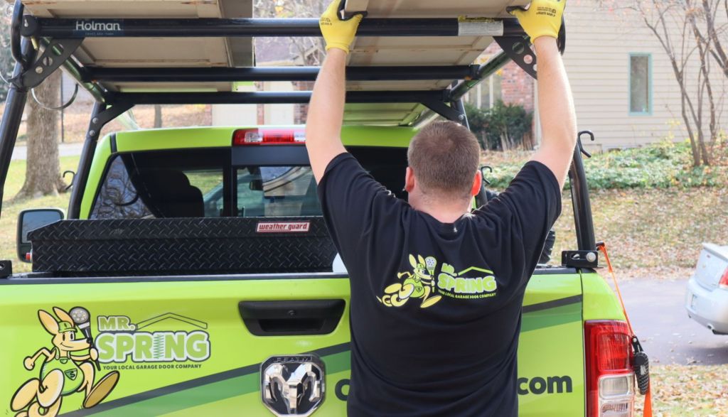 garage door repair technician loads supplies into rack of bright green Mr. Spring pickup truck