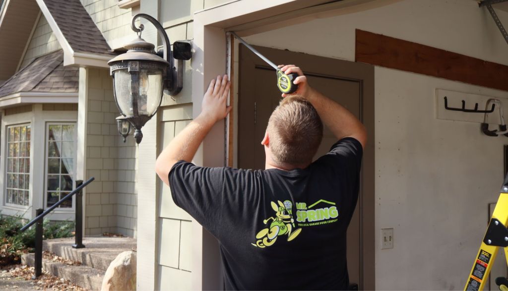 A Mr. Spring repair technician measures an exterior garage door frame