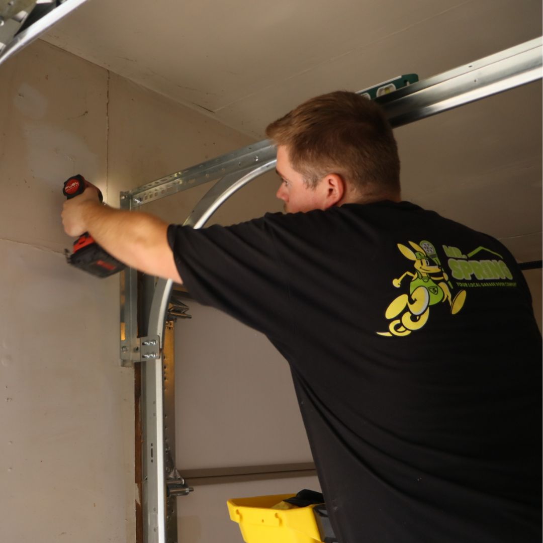 a Mr. Spring technician uses a screw gun to secure a new garage door track bracket