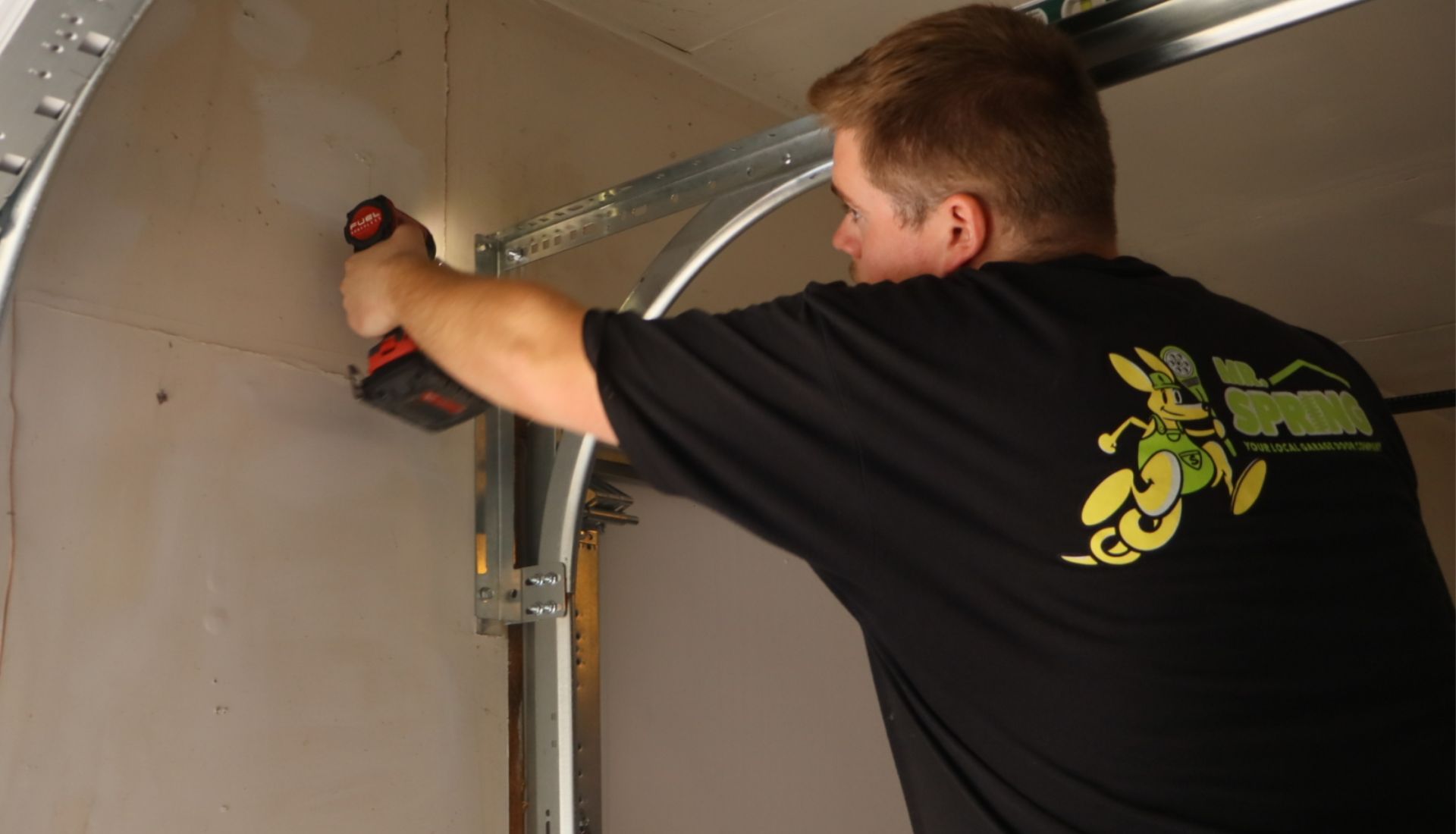 a Mr. Spring technician uses a screw gun to secure a new garage door track bracket