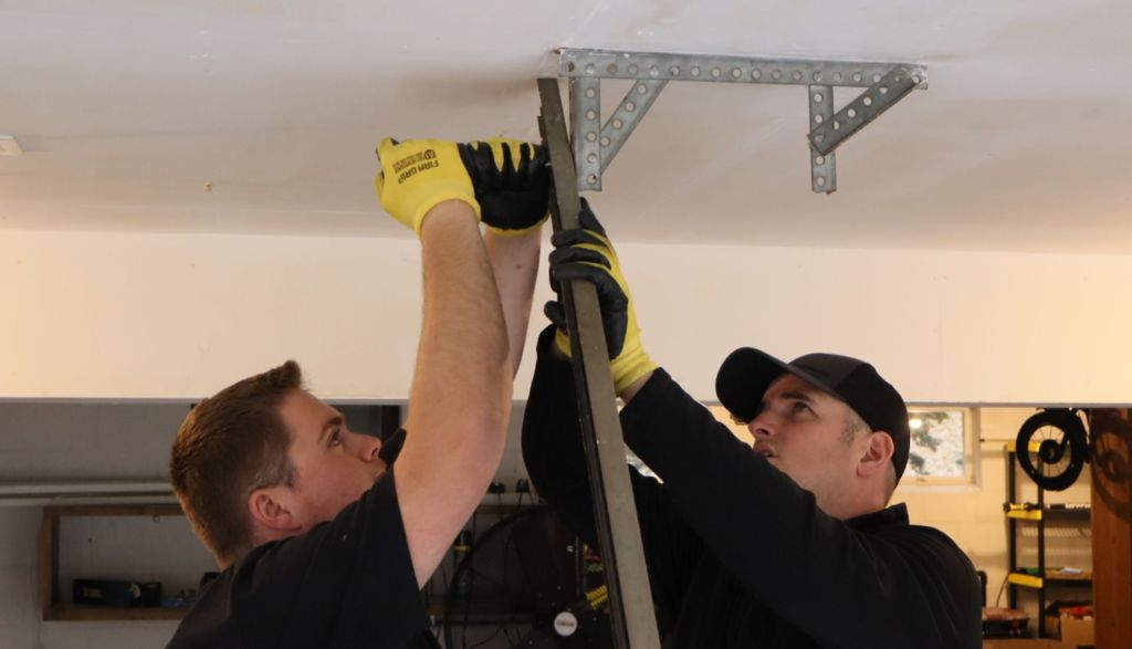 two garage door repair technicians work together to secure a new ceiling bracket