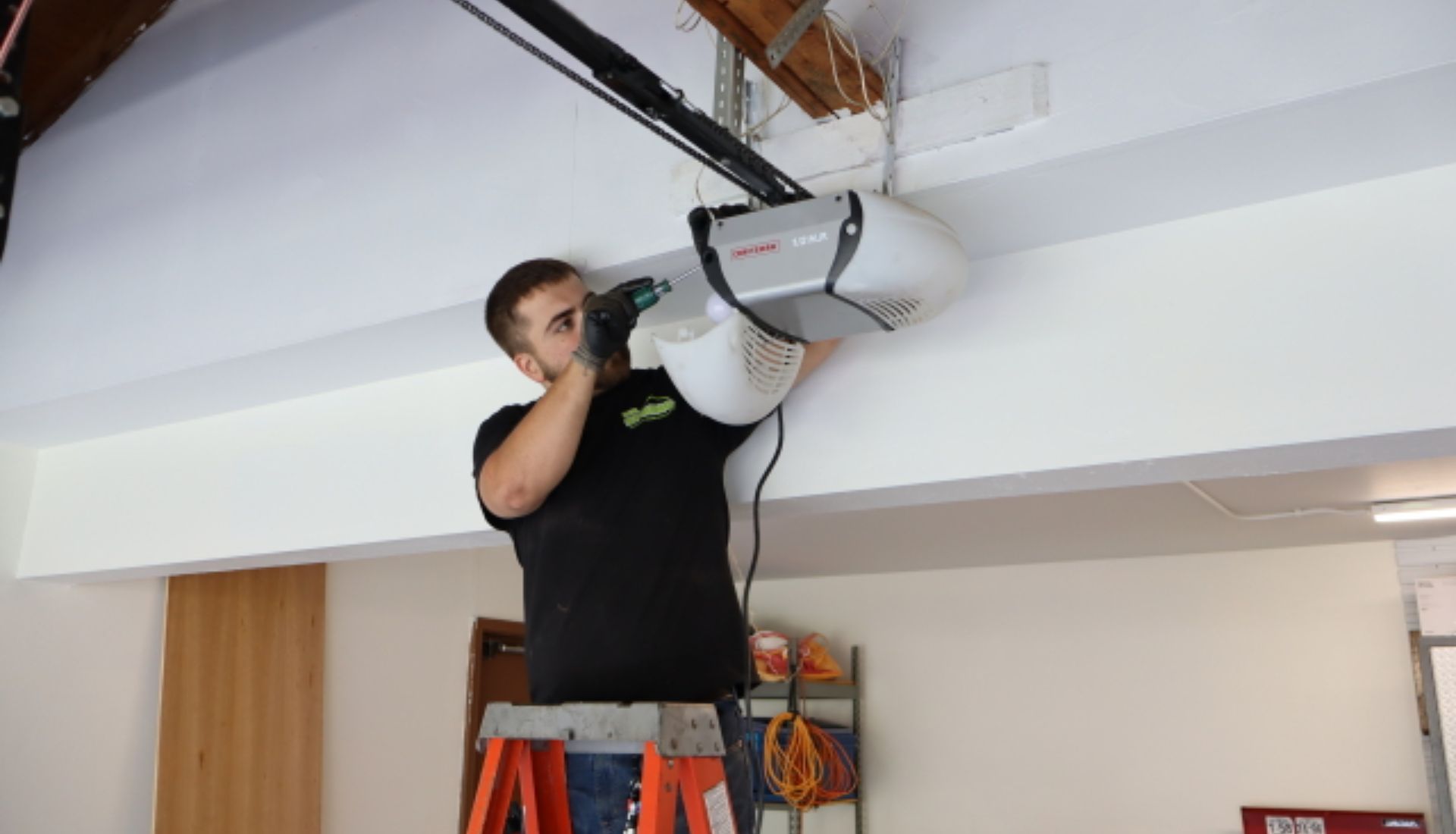 a Mr. Spring technician stands on an orange ladder to change the light bulb under the cover of a garage door opener