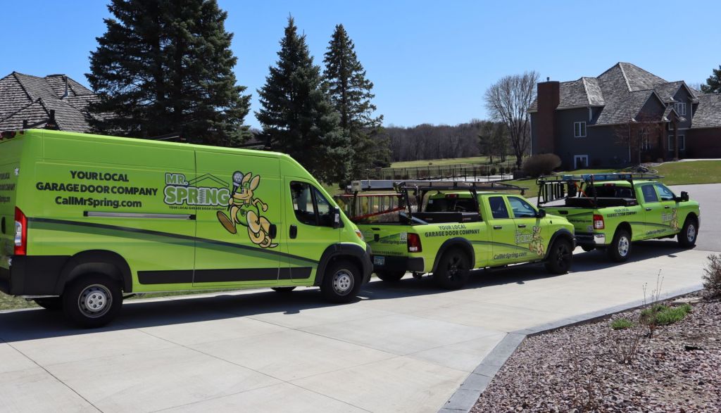 three bright green Mr. Spring vehicles sit in a line in a suburban driveway