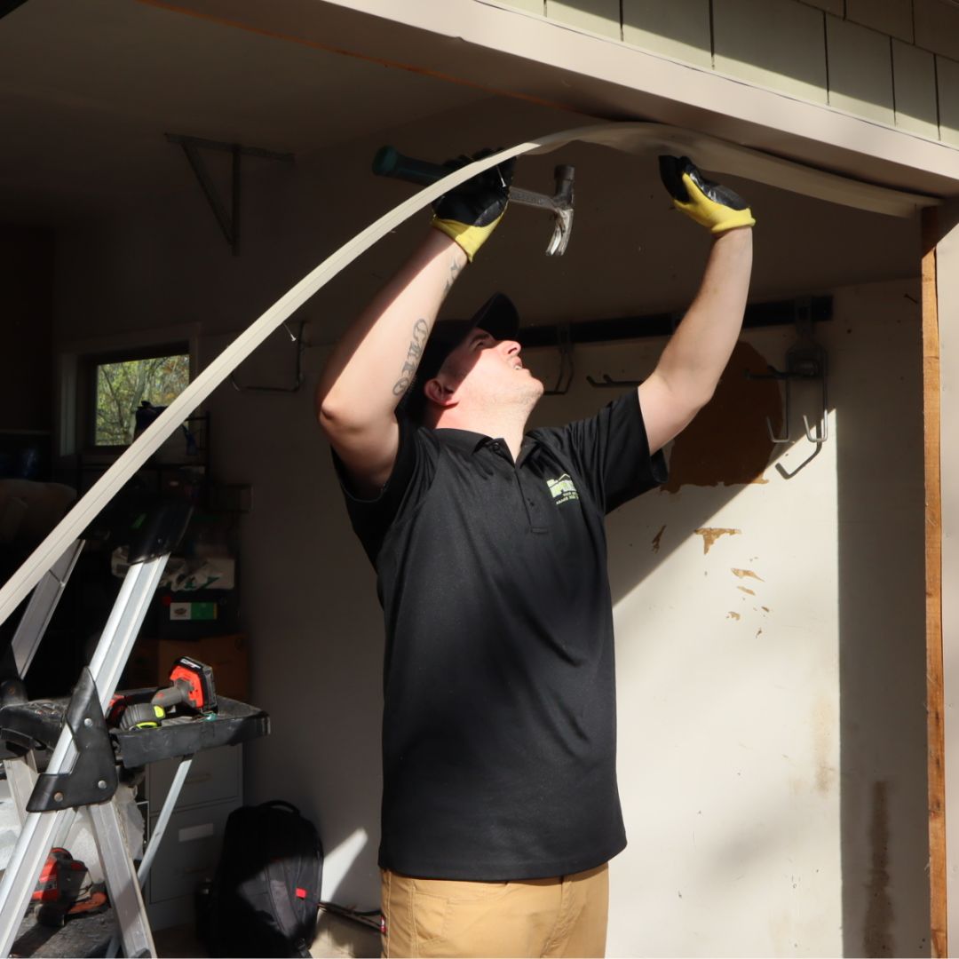 Mr. Spring technician reaches overhead to hammer new trim to the top of an open garage door frame