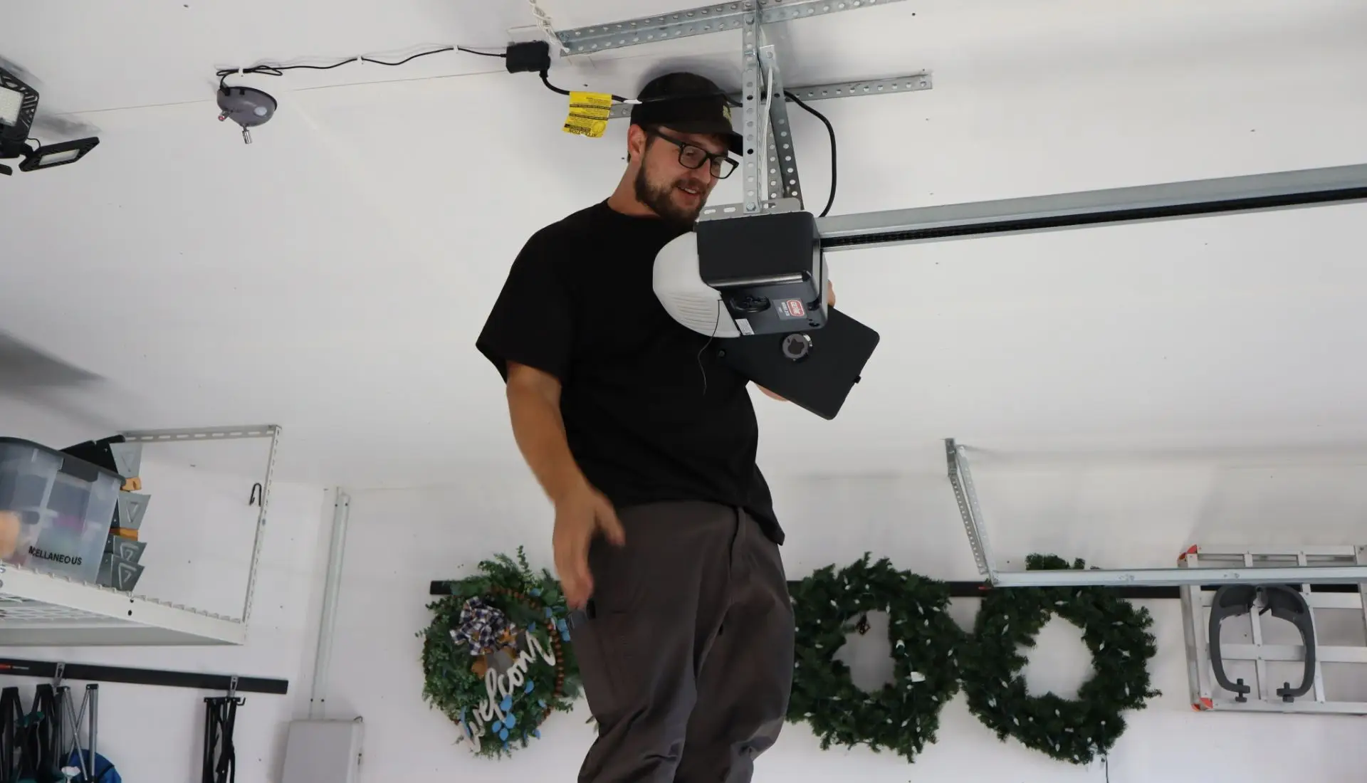 repair technician stands on a ladder to examine a garage door opener