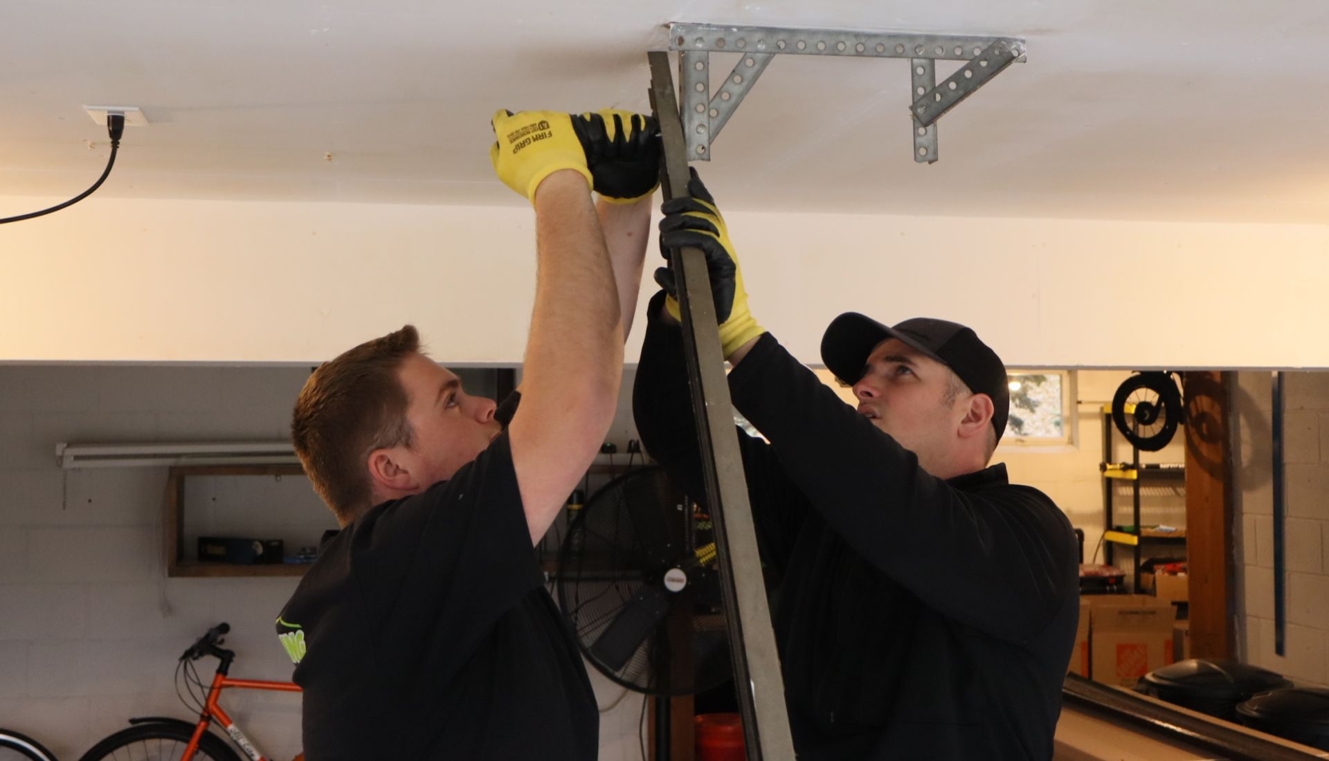 Two Mr. Spring techs removing garage door tracks from a ceiling bracket