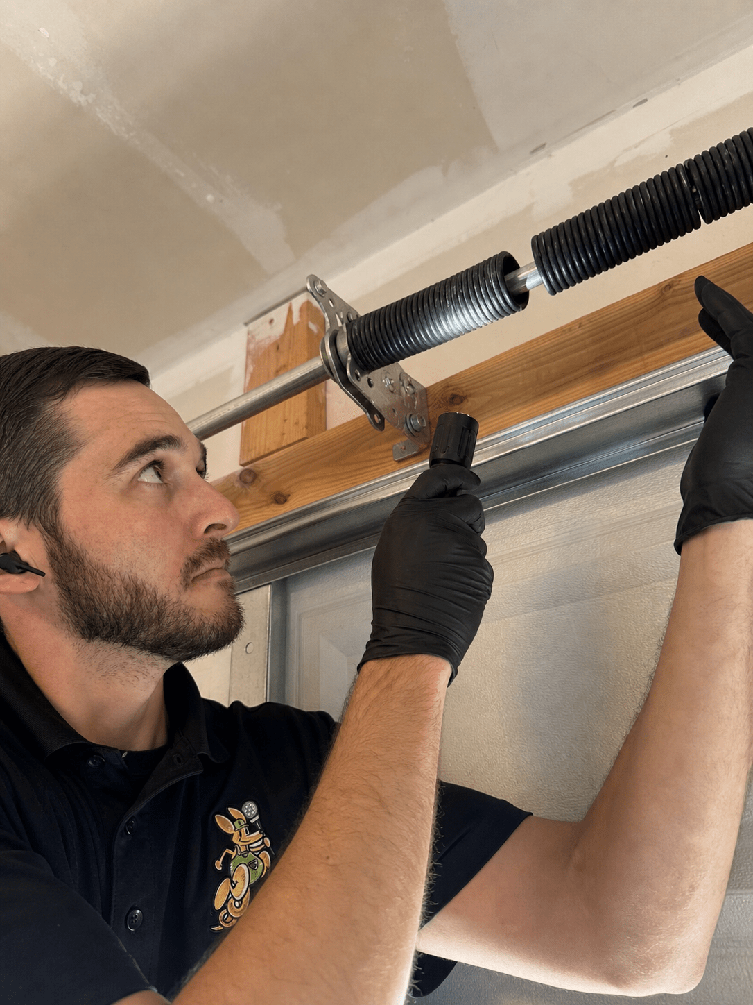 Mr. Spring technician inspecting a garage door torsion spring above the track before repair