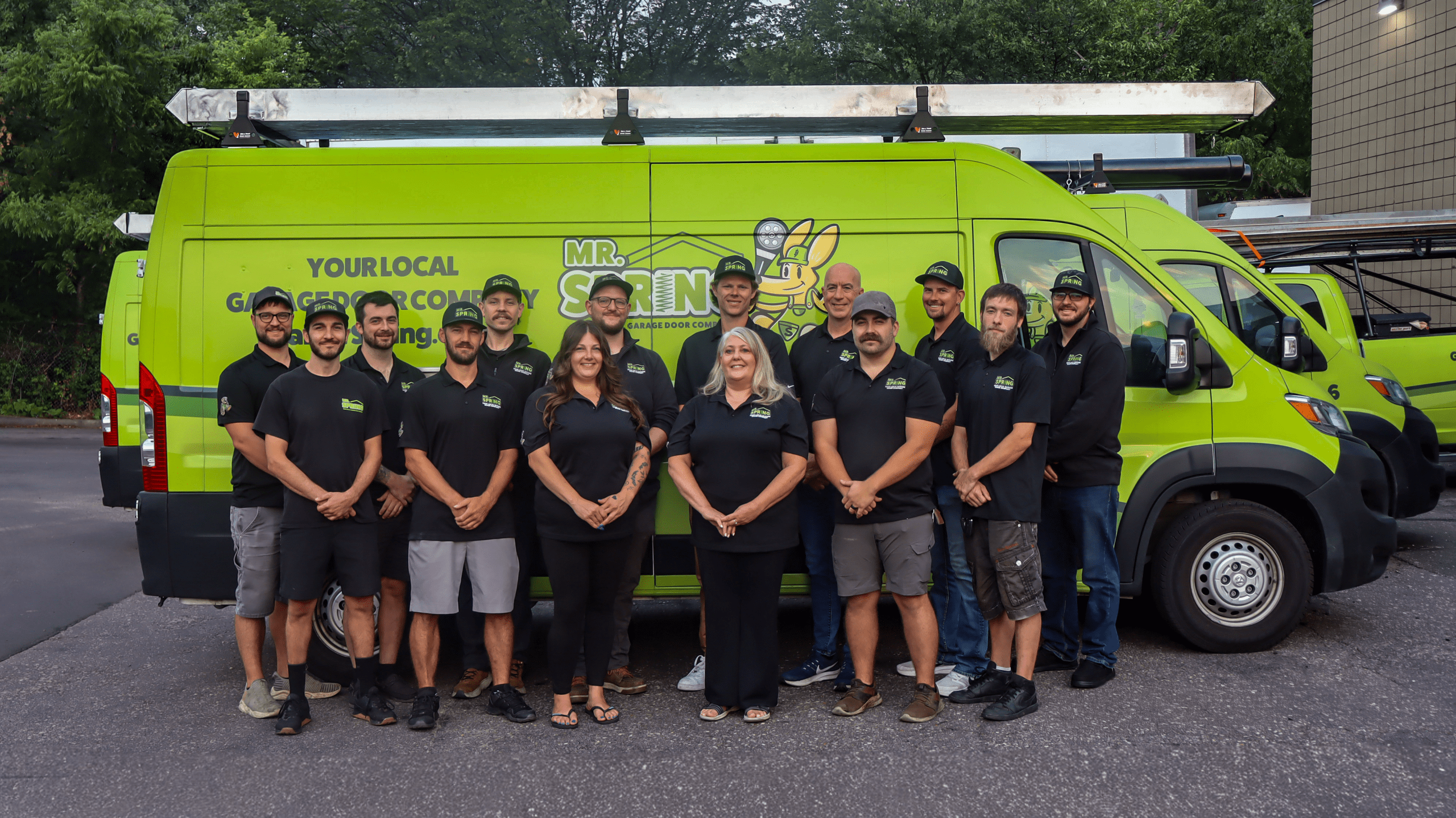 Mr. Spring Garage Door Company team standing in front of bright green service vans with ladders mounted on top.